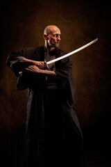 View of a blind and bald man wearing a kimono holding a katana in his hands