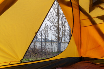 Looking outside of a yellow tent while camping in northern Canada with dry, spring time trees waiting to bloom for the summer on cloudy afternoon. Raining camp. 