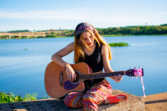 hermosa mujer hippie tocando la guitarra a la orilla de un rio 