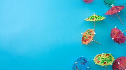 Festive cocktails, decorating tropical drinks and summer party concept with repetitive pattern of  colourful decorative paper cocktail umbrellas isolated on blue background with copy space