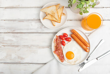 Plate of breakfast with fried eggs, bacon,sausages and toasts bread with orange juice on white wood table.