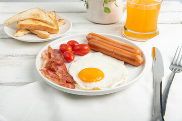 Moning breakfast with fried eggs, sausages,tomatoes,orange juice and bacon on white wood table.