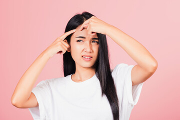 Portrait teenage Asian beautiful young woman having skin problems squeezing pimples on her face, studio shot on pink background, with copy space, Thai female acne, beauty care concept