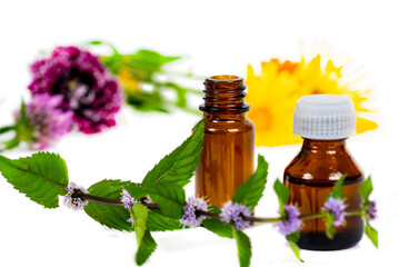 brown bottles with flowered mint branch and marigold flowers on white background
