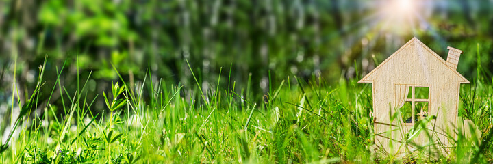 The symbol of a wooden eco-house among the green grass in the forest. The concept of ecological balance, nature protection and human health. Panoramic view