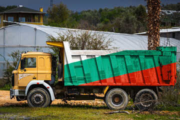 Obraz premium Dump truck with the image of the national flag of Bulgaria is parked against the background of the countryside. The concept of export-import, transportation, national delivery of goods