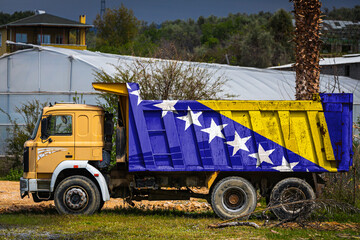 Dump truck with the image of the national flag of Bosnia Herzegovina is parked against the background of the countryside. The concept of export-import, transportation, national delivery of goods