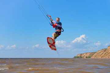 Kiteboarder surfing waves with kiteboard on a sunny summer day. A man performs a trick-jump on a surfboard.