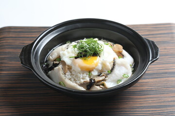 chef cook Hong Kong congee porridge with mixed seafood unagi, fish, prawn, squid, mushroom, egg and vegetables in black hot clay pot , chopstick spoon asian healthy halal menu