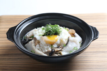 chef cook Hong Kong congee porridge with mixed seafood unagi, fish, prawn, squid, mushroom, egg and vegetables in black hot clay pot , chopstick spoon asian healthy halal menu