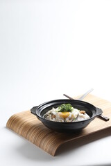 chef cook Hong Kong congee porridge with mixed seafood unagi, fish, prawn, squid, mushroom, egg and vegetables in black hot clay pot , chopstick spoon asian healthy halal menu