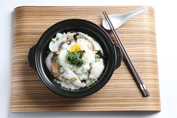 chef cook Hong Kong congee porridge with mixed seafood unagi, fish, prawn, squid, mushroom, egg and vegetables in black hot clay pot , chopstick spoon asian healthy halal menu