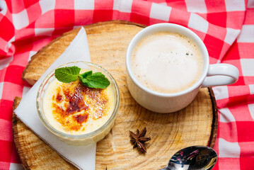Creme brulee dessert portion garnished with mint leaves in a glass Ramekin form on a wooden board and with a checkered red-white napkin on a side