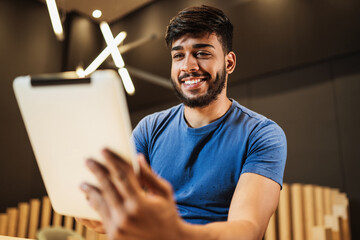 Young latin man using digital tablet. Texting on cafe.