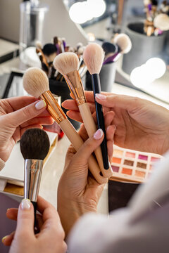 Close up hands of female makeup artist studying client choosing brush for cosmetics applying