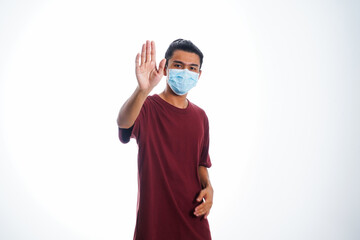 Covid19, the concept of health care and medicine. A young man standing in a face mask with hand gesture "stop", supporting social distance