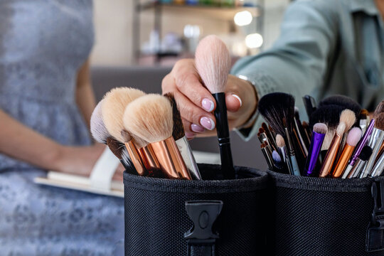 Closeup female makeup artist hands taking brush for applying cosmetics explaining to client