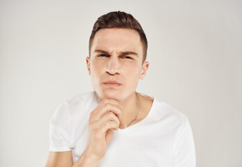 a man with a serious expression that in a white t-shirt suspicious look light background