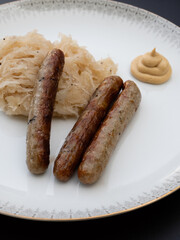 Nuremberg Grilled Sausage or Nürnberger Rostbratwurst with Sauerkraut or Sour Cabbage and Mustard on a White Plate Vertical Orientation