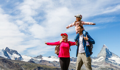 Happy family with little child doing trekking on switzerland mountain in summer time. Young people...