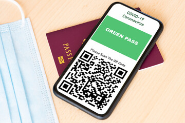 A passport and a smartphone with a Green Pass are arranged on a wooden table. 