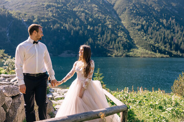 The bride and groom by the lake in the mountains. A couple together against the background of a mountain landscape is walking up the stairs holding hands.