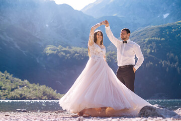 Bride and groom on the shore of the lake with a beautiful view of the mountains. The newlyweds in...