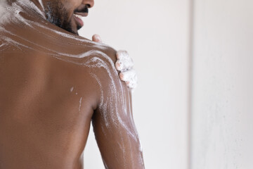 Muscular back of mixed race African bearded guy, taking shower, applying foamy gel or soap on smooth dark skin. Male morning bath routine, daily hygiene, bodycare concept. Cropped shot, close up - obrazy, fototapety, plakaty