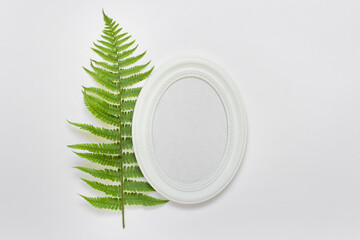 Mockup template with vertical oval frame and green fern leaf on white background.