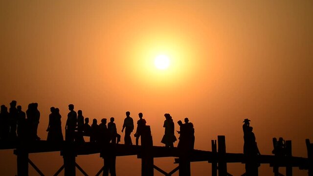 people in silhouette walking on sun set U-Bein bridge, Myanmar