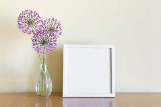 Mockup template of square white frame standing on wooden shelf with summer purple flowers.