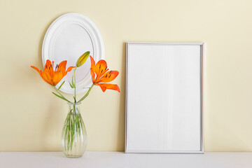Two frames A4 and oval white frame with orange summer lily in glass vase on yellow wall background.
