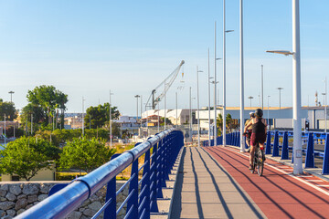 Metal bridge with some cyclists, and the port of Gandia in the background. 