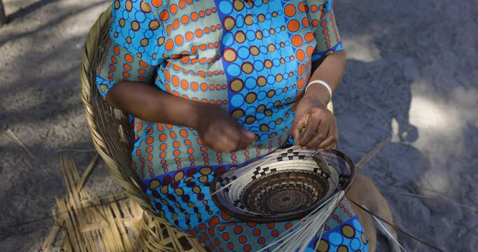 Close-up cropped view of a woman weaving a traditional basket made from the fan palm leaf fibre
