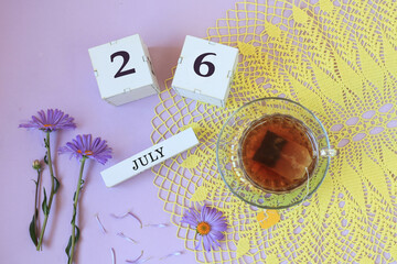Calendar for July 26: cubes with the number 26, the name of the month of July in English , a cup of tea on a yellow openwork napkin, flowers on a pastel background