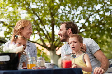 mother and father with their children in laps sitting outdoor, looking each other, smiling