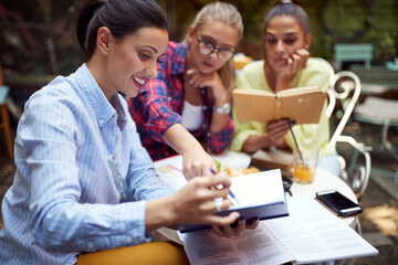 three young adult women studying together in outdoor cafe.