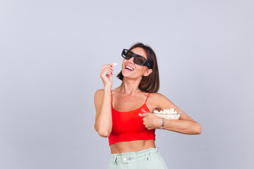 Beautiful woman on gray background in 3d cinema glasses with popcorn, cheerful happy positive emotions