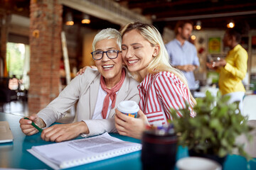 Female colleagues in a hug are posing for a photo in the office
