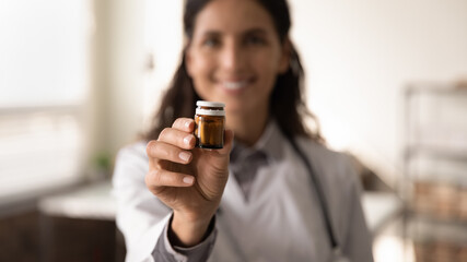 Crop close up blurred background of female doctor hold bottle medication prescribe pills to sick patient. Woman GP or therapist recommend good quality medicines. Healthcare, treatment concept.
