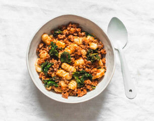Potatoes gnocchi  with bolognese sauce and kale on a light background, top view - obrazy, fototapety, plakaty