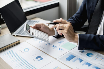 A man with a pen pointing to a white calculator and documents are placed on the table, a...