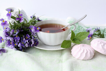 Obraz na płótnie Canvas Bouquet of violets, a cup of tea, homemade marshmallows. Romantic morning. Selective focus.