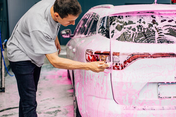 Detailed view of a car wash, car wash with foam, a man washes the headlights of a car with a...