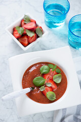 Gazpacho soup with addition of fresh strawberry, vertical shot on a light-grey marble background, elevated view