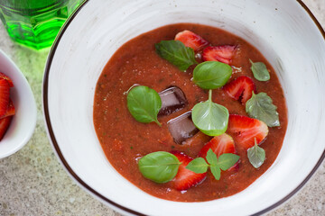 Closeup of a white bowl with cold strawberry and tomato soup gazpacho, elevated view, selective focus