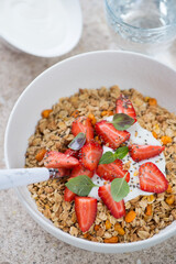Closeup of of granola topped with fresh strawberries and yogurt in a white bowl, vertical shot, selective focus