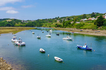Fototapeta na wymiar Estuary of the sea with small boats anchored and blue sky in summer. San Vicente de la Barquera.