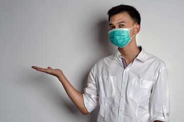 Attractive young asian man wearing a health mask with right hand open gesture against white background. Prevention of the spread of corona virus photography concept. Novel Coronavirus (COVID-19)