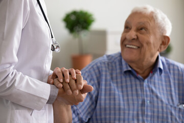 Close up of female nurse in white uniform hold happy mature male patient hand show good medical...
